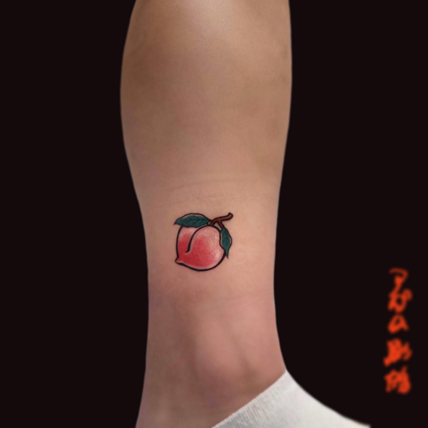 A small tattoo of a peach with leaves on an ankle
